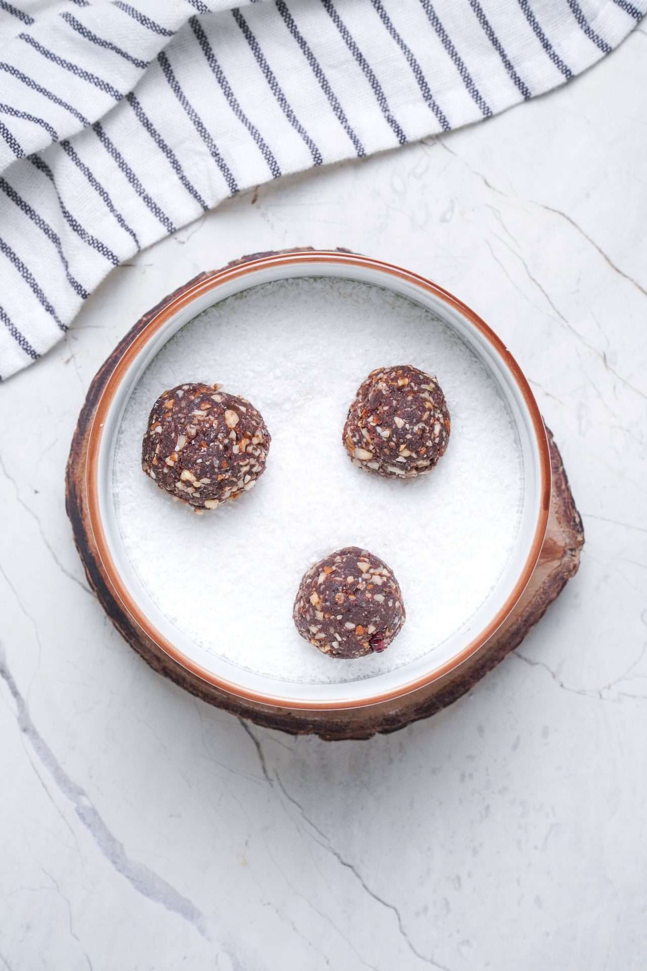 Healthy chocolate truffles made with nuts and medjool dates. Sitting in a bowl of desiccated coconut.