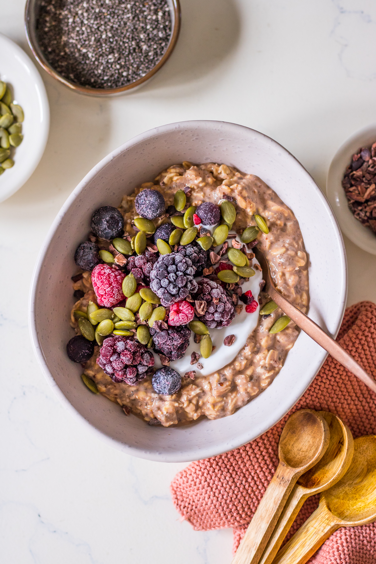 Bowl of overnight oats with cacao, yoghurt, frozen berries and pumpkin seeds