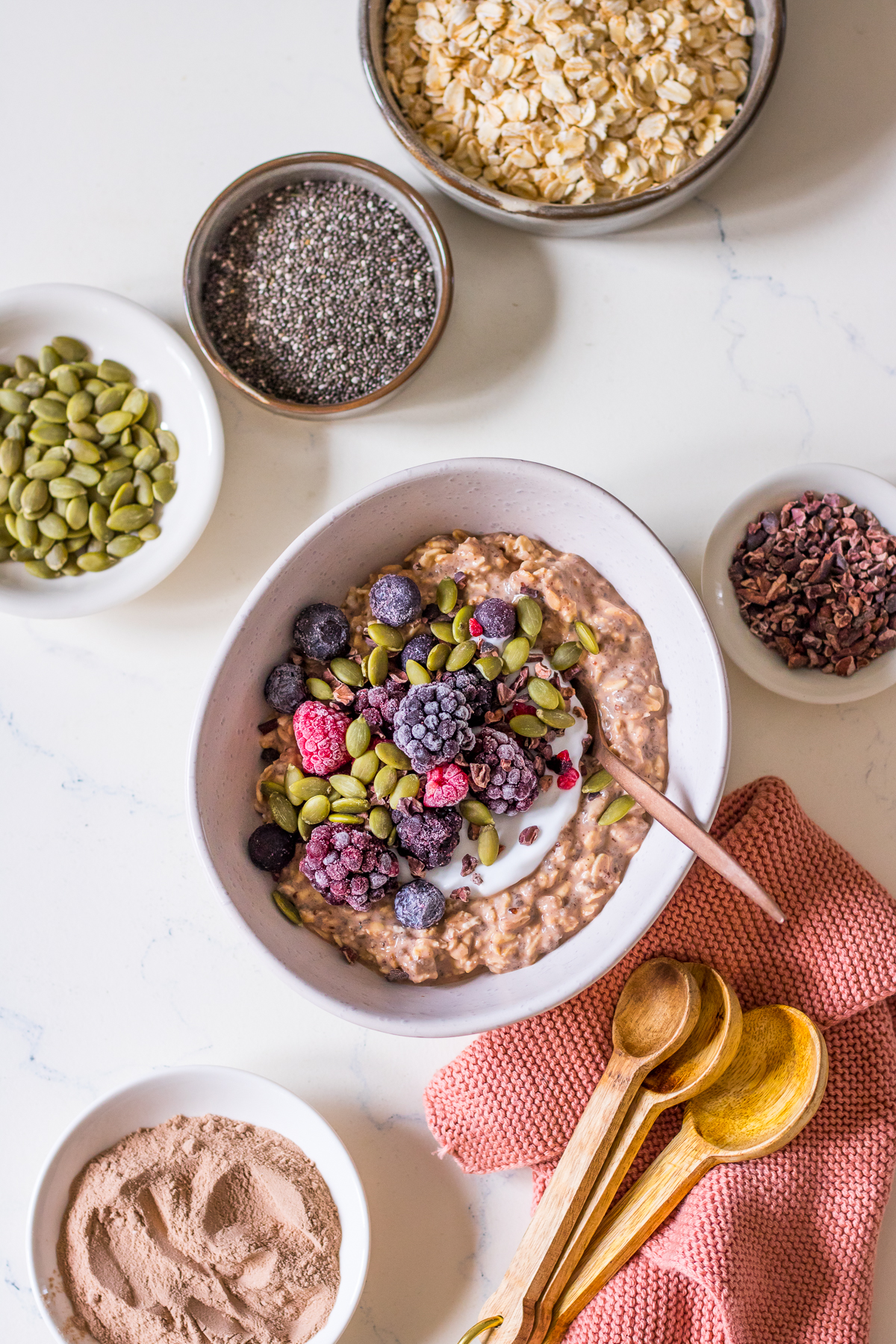 Chocolate protein overnight oats with chia seeds in a white bowl, topped with frozen berries and seeds