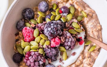 Small white ceramic bowl with chocolate protein overnight oats, yoghurt, berries, cacao nibs and pumpkin seeds