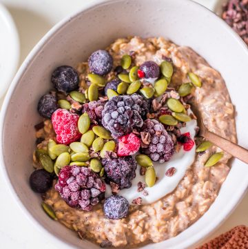 Small white ceramic bowl with chocolate protein overnight oats, yoghurt, berries, cacao nibs and pumpkin seeds