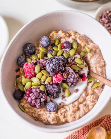 Small white ceramic bowl with chocolate protein overnight oats, yoghurt, berries, cacao nibs and pumpkin seeds