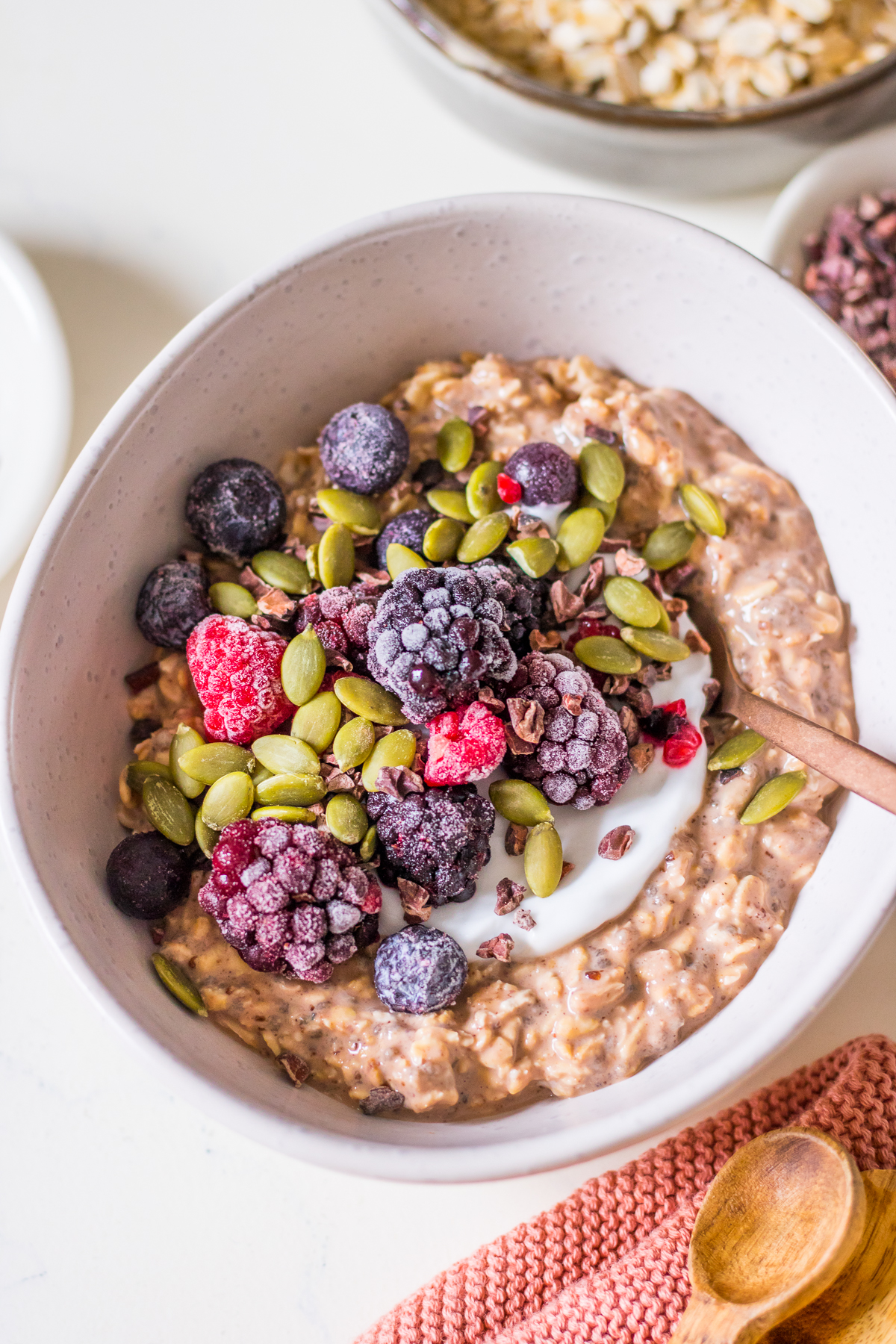 White ceramic bowl close up with chocolate oats, chia seeds, yoghurt, frozen berries and pumpkin seeds