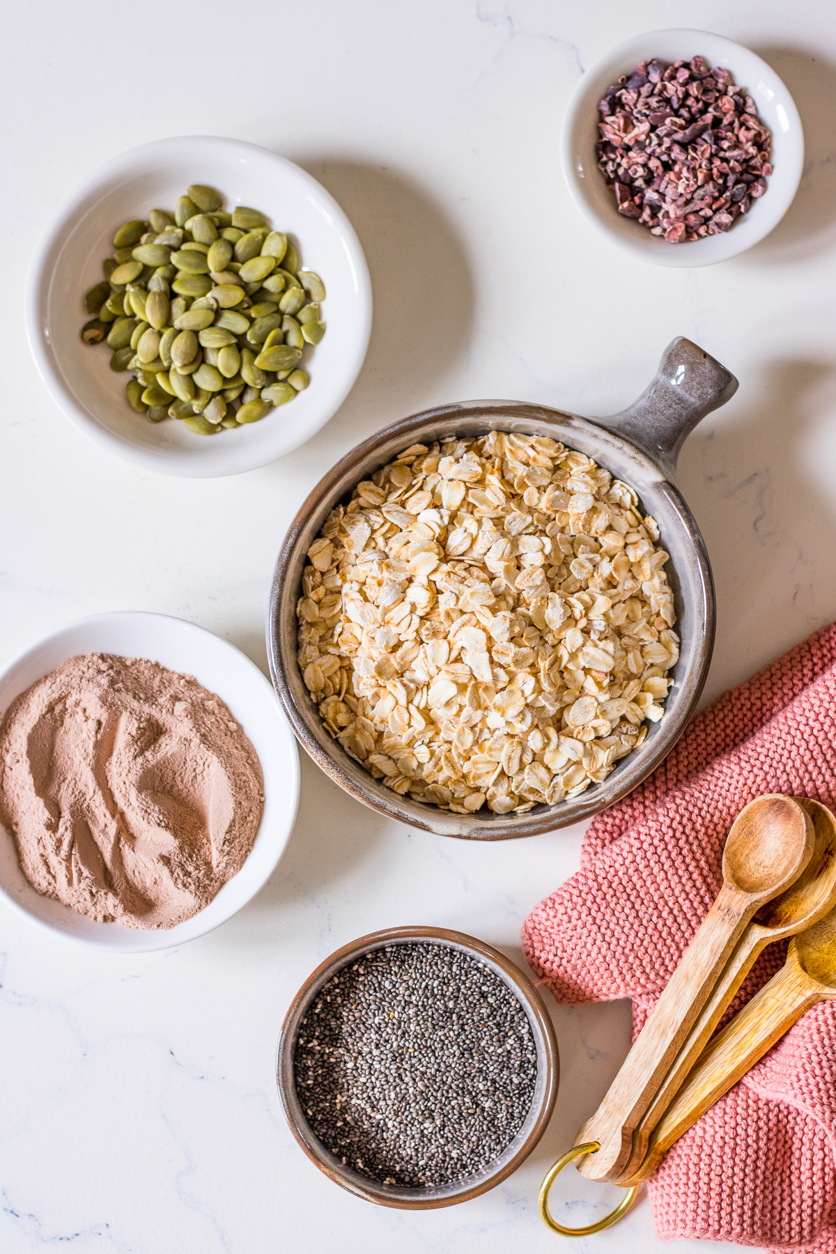 Small ceramic round dishes with rolled oats, pumpkin seeds, cacao nibs, chocolate protein powder, chia seeds