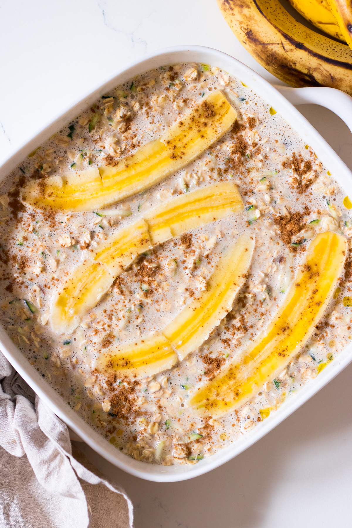 Square white baking dish with oats, grated zucchini, banana, cinnamon