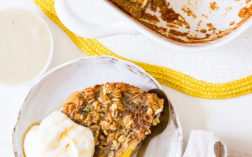 Baked oats in a square white baking dish with banana on top, and a side plate of baked oats with yoghurt