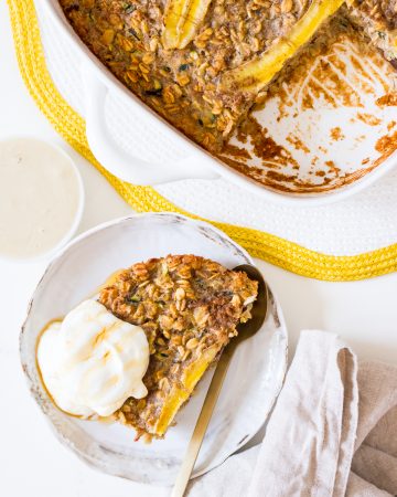 Baked oats in a square white baking dish with banana on top, and a side plate of baked oats with yoghurt