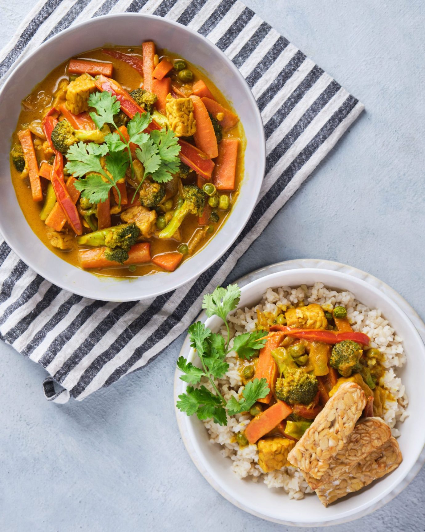 Vegetable yellow curry with tempeh strips served in bowls with brown rice
