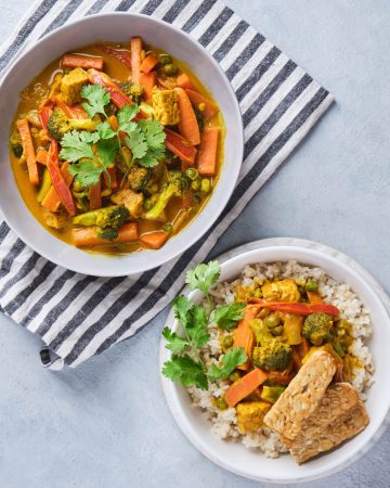 Vegetable yellow curry with tempeh strips served in bowls with brown rice