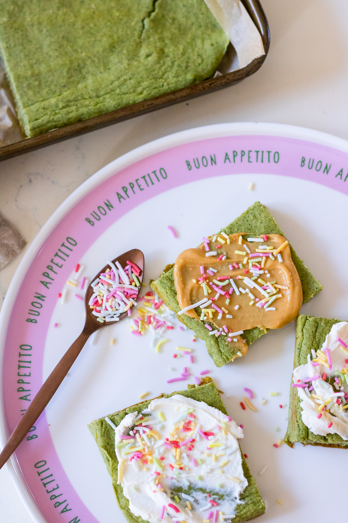 Image of green pancakes cut into square shape topped with peanut butter or cream cheese and rainbow sprinkles