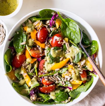 Image of a tuna salad with baby spinach, capsicum, cabbage and cherry tomatoes in a speckled white bowl