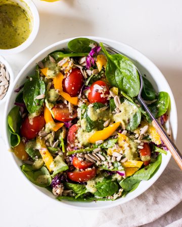 Image of a tuna salad with baby spinach, capsicum, cabbage and cherry tomatoes in a speckled white bowl