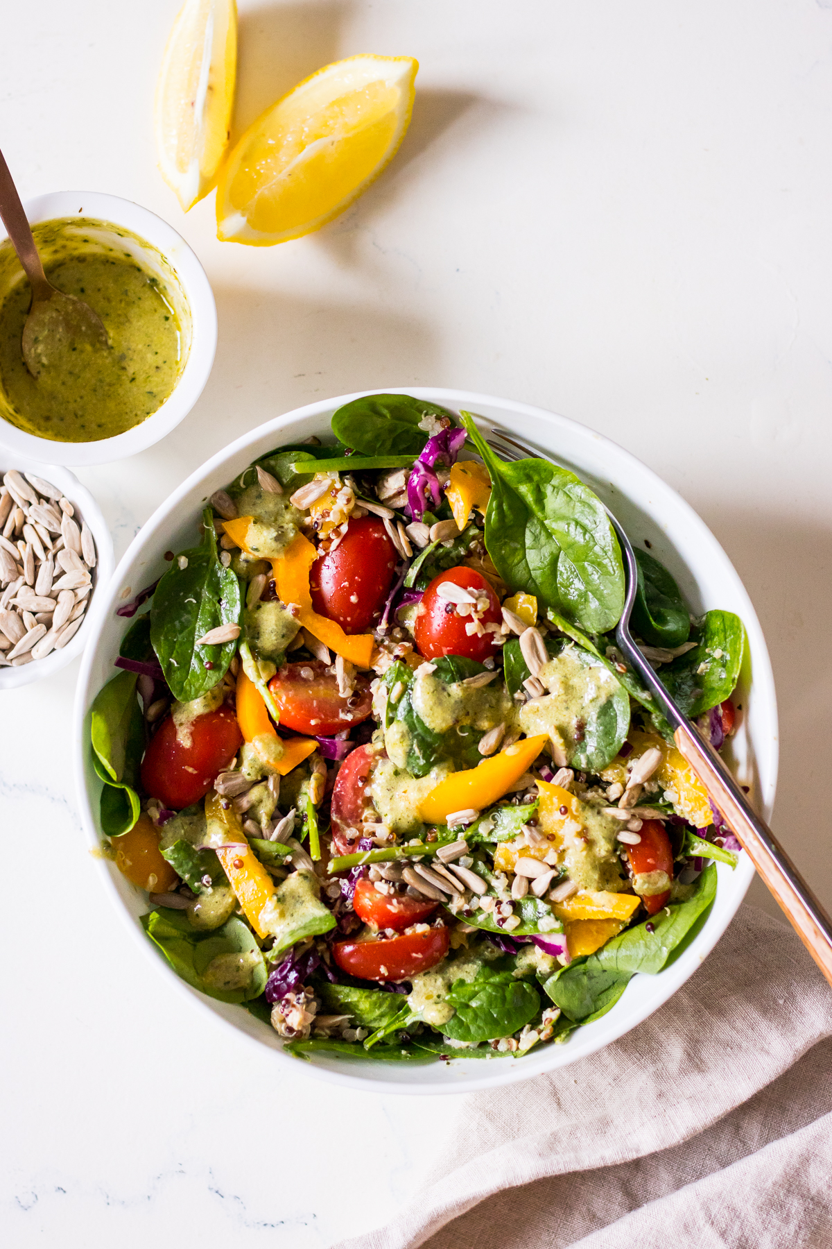 An image of a spinach and quinoa tuna salad with pesto dressing in a white bowl with pesto dressing and lemon wedge on the side