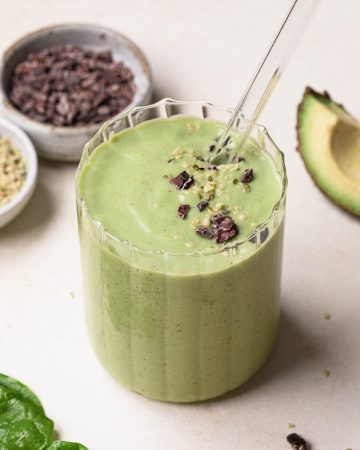 Avocado, banana and spinach green smoothie in a clear glass with a glass straw