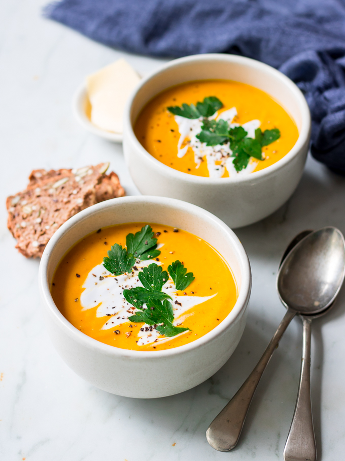 Two ceramic bowls filled with coconut pumpkin soup garnished with fresh herbs