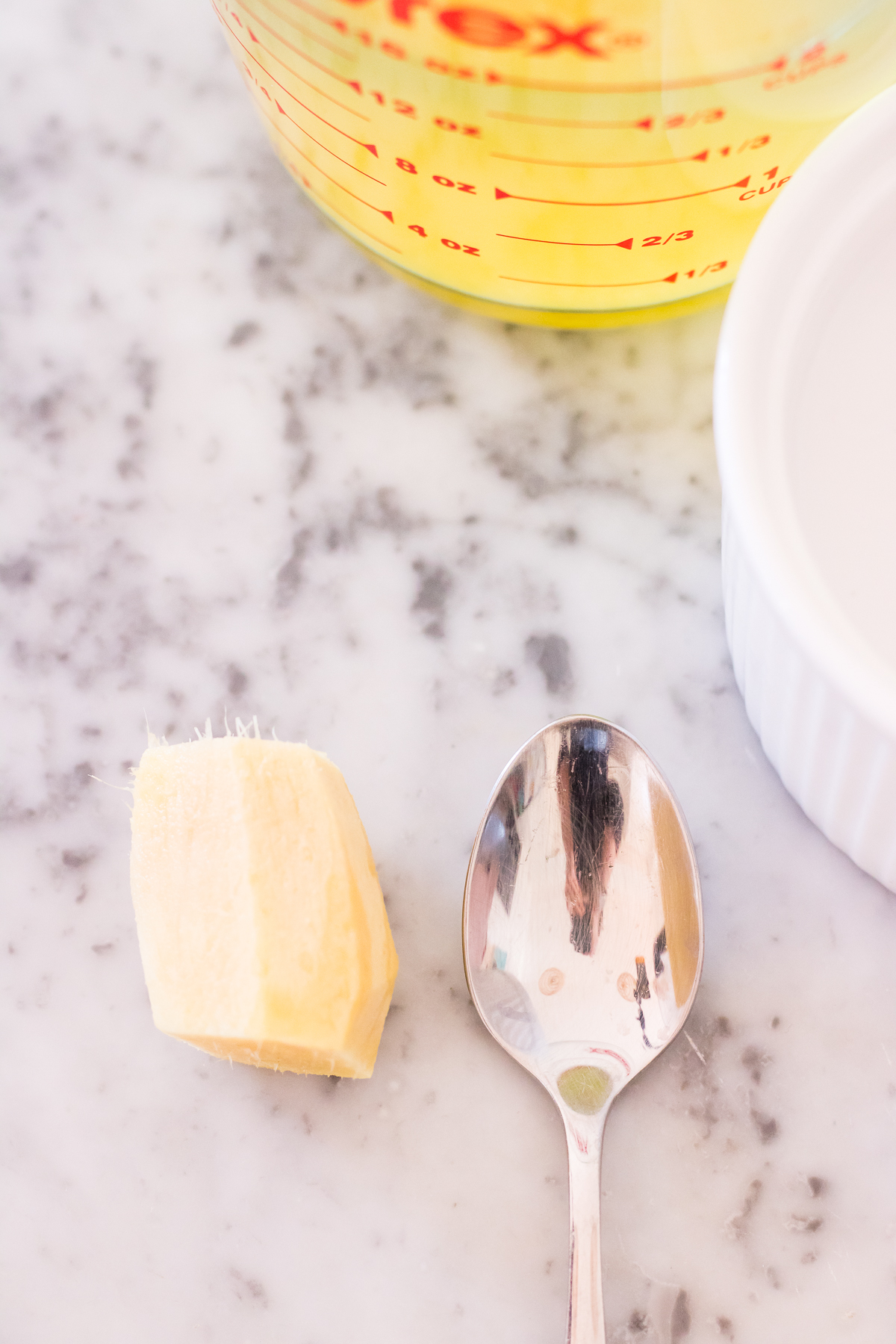 Image of a peeled piece of fresh ginger next to a teaspoon