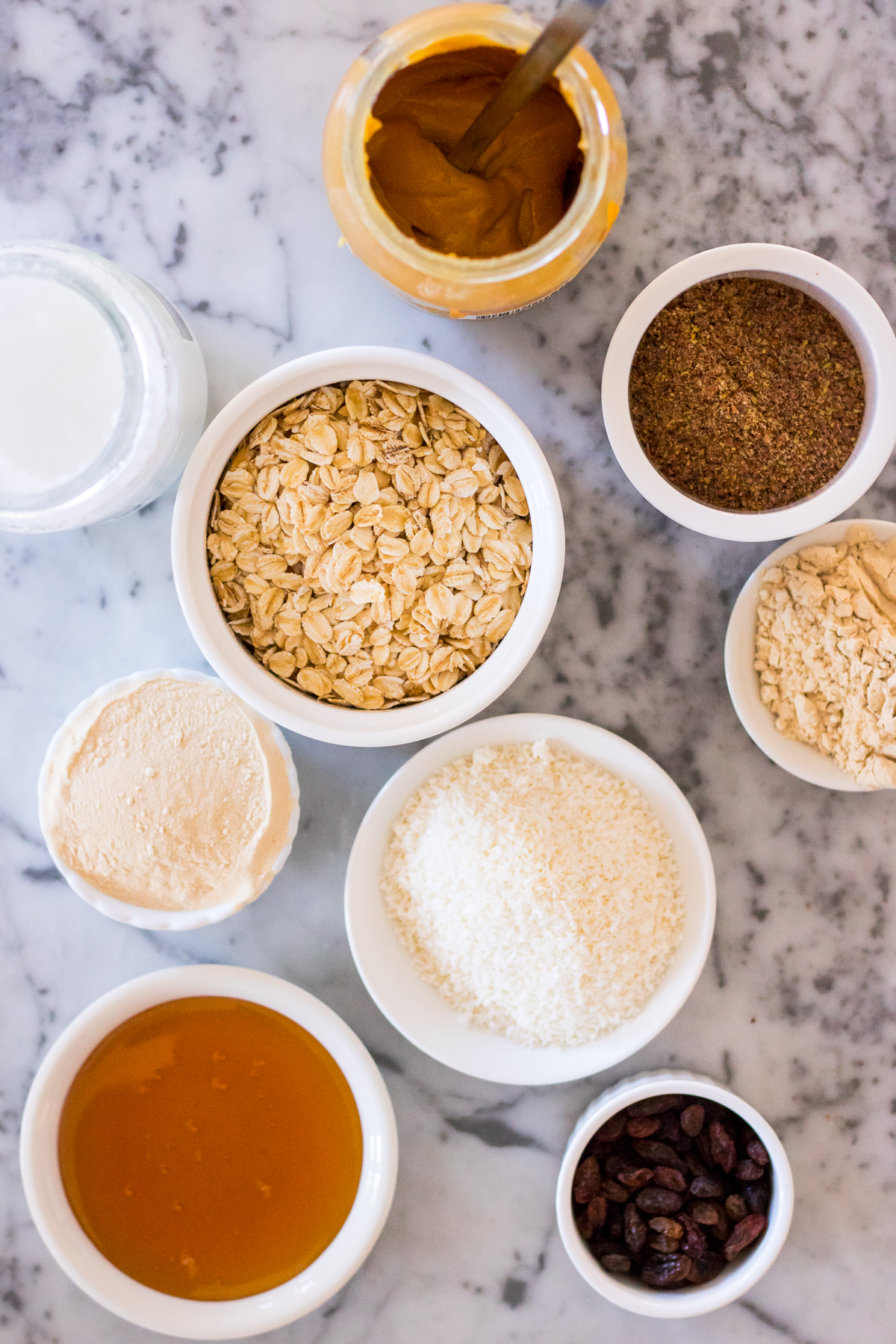Ingredients to make lactation energy balls arranged into small ceramic dishes on a marble background