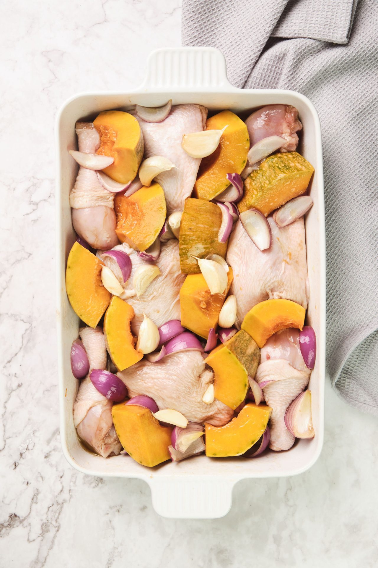 White baking dish with chicken, onion, pumpkin and garlic cloves