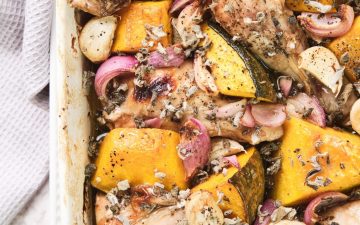 White roasting dish with roast chicken, onion, garlic and sage
