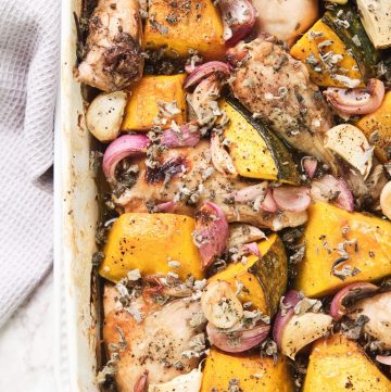 White roasting dish with roast chicken, onion, garlic and sage