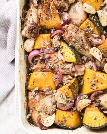 White roasting dish with roast chicken, onion, garlic and sage