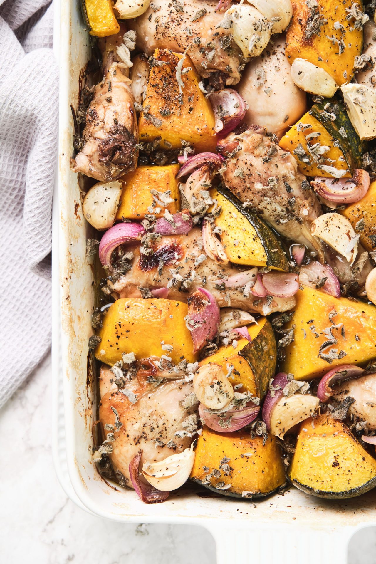 White roasting dish with roast chicken, onion, garlic and sage