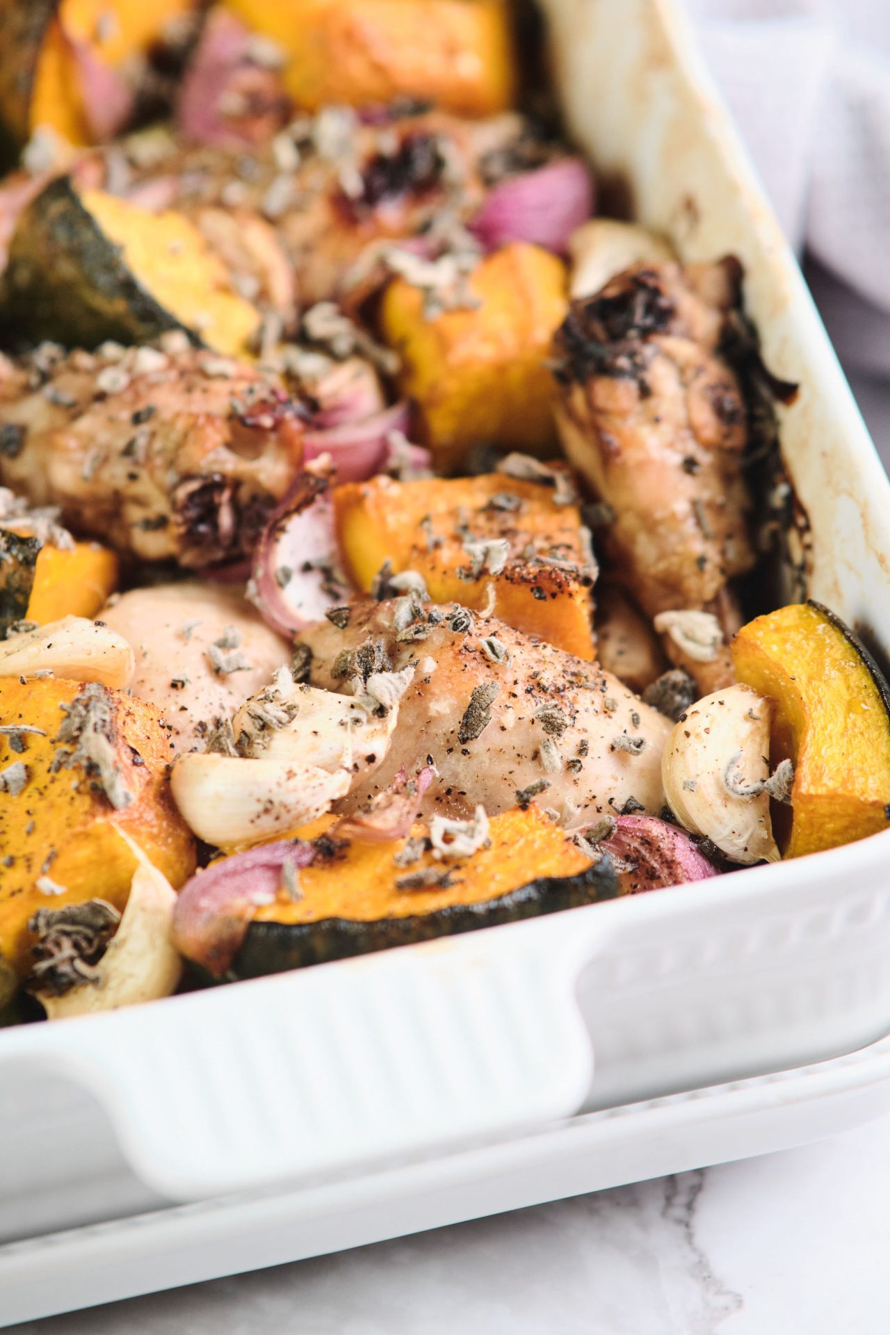 White baking dish with roast chicken, pumpkin, garlic, onion and herbs