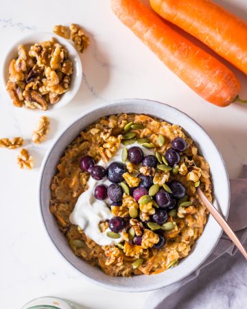 Carrot cake oatmeal topped with Greek yoghurt, blueberries and walnuts in a small bowl