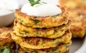 Stack of gluten free corn fritters on a white plate topped with yoghurt and herbs.