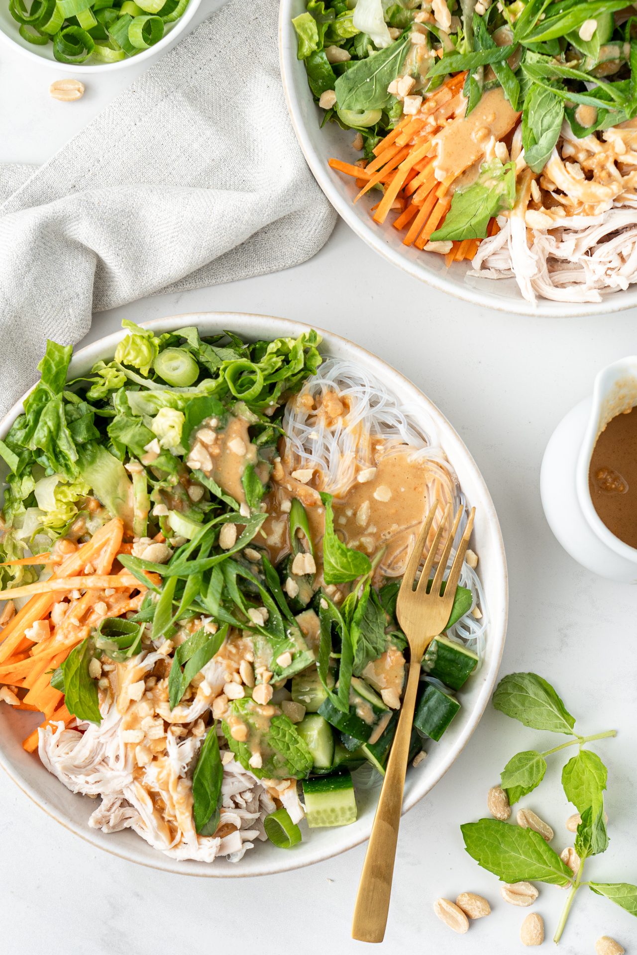 Bowls with vermicelli noodles, vegetables, fresh herbs and peanut butter sauce spread on top | Nourish Every Day