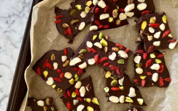 Dark chocolate bark topped with chopped pistachios, macadamias and goji berries, set on a baking tray lined with parchment paper