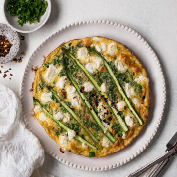 Pea and asparagus omelette on a white plate with silver cutlery, overhead shot