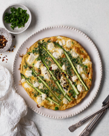 Pea and asparagus omelette on a white plate with silver cutlery, overhead shot