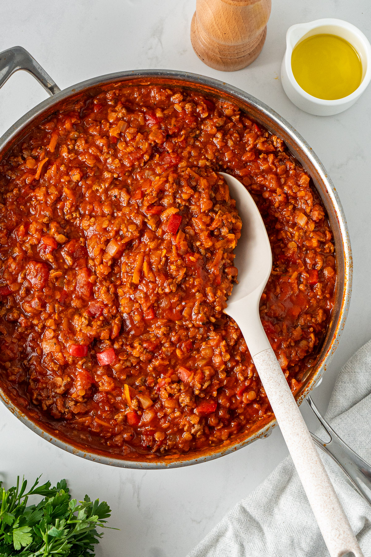Homemade healthy bolognese sauce made with mince, red lentils and vegetables, shown in a stainless steel pan with a spoon.