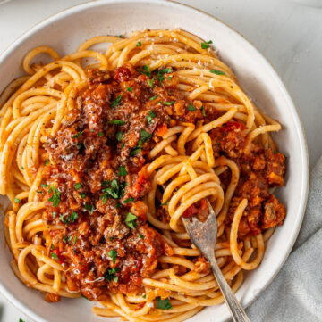 A bowl of beef bolognese with red lentils served over spaghetti, topped with freshly grated parmesan