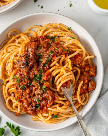 A bowl of beef bolognese with red lentils served over spaghetti, topped with freshly grated parmesan