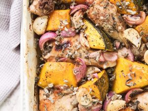White roasting dish with roast chicken, onion, garlic and sage