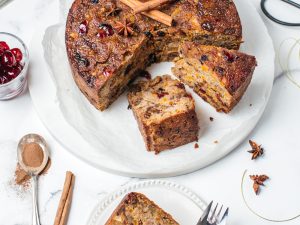 Christmas fruit cake on a white plate partly sliced, one slice on a side plate with fork