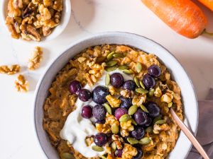 Carrot cake oatmeal topped with Greek yoghurt, blueberries and walnuts in a small bowl